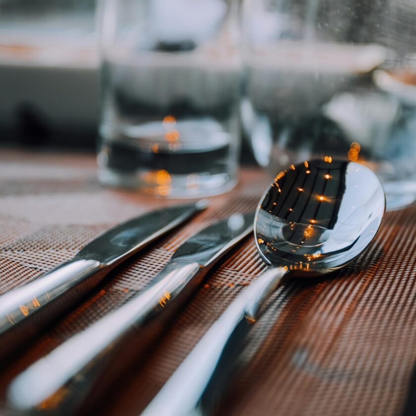 A close-up shot of shiny silver cutlery on a table, reflecting warm lighting.