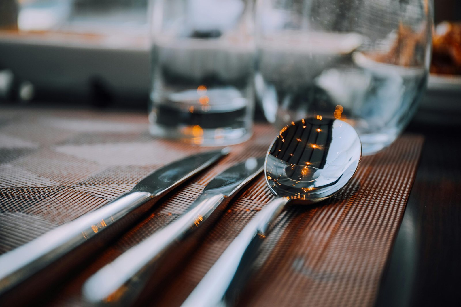 A close-up shot of shiny silver cutlery on a table, reflecting warm lighting.